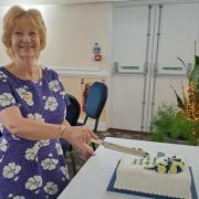 Chair Corinne Halkyard cutting the celebratory cake for West Wight Floral Arts Society